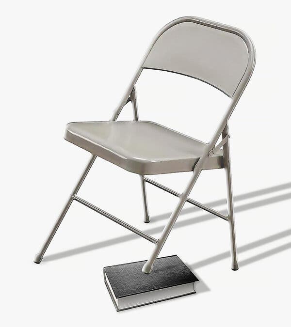 This image shows a gray metal folding chair with a hardback book under one leg.