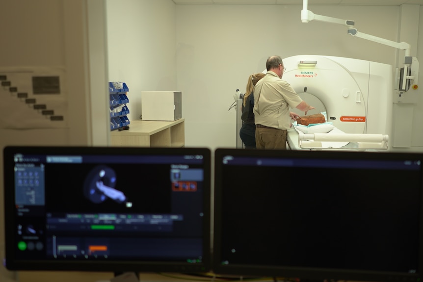 A computer screen sits in front of a window showing a CT scanner